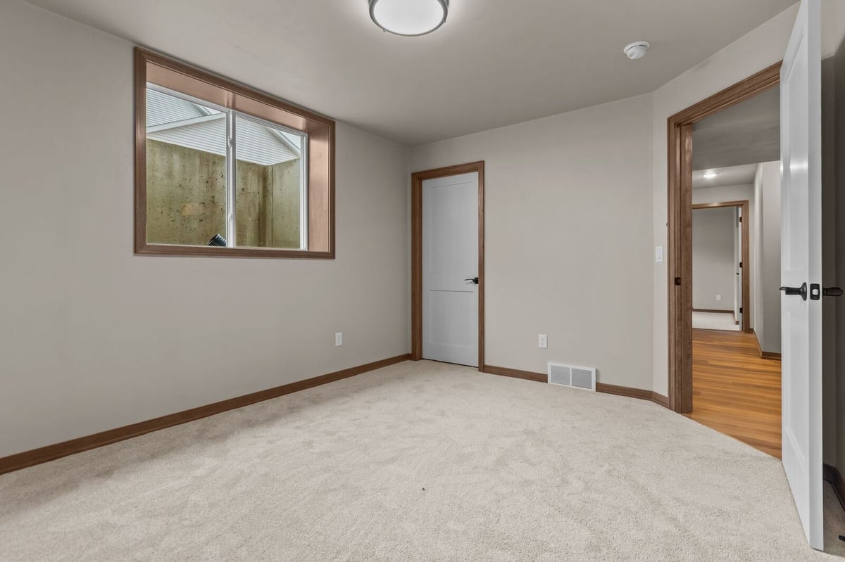 Lower-level bedroom with soft carpet and hallway access in a Northern Wisconsin home