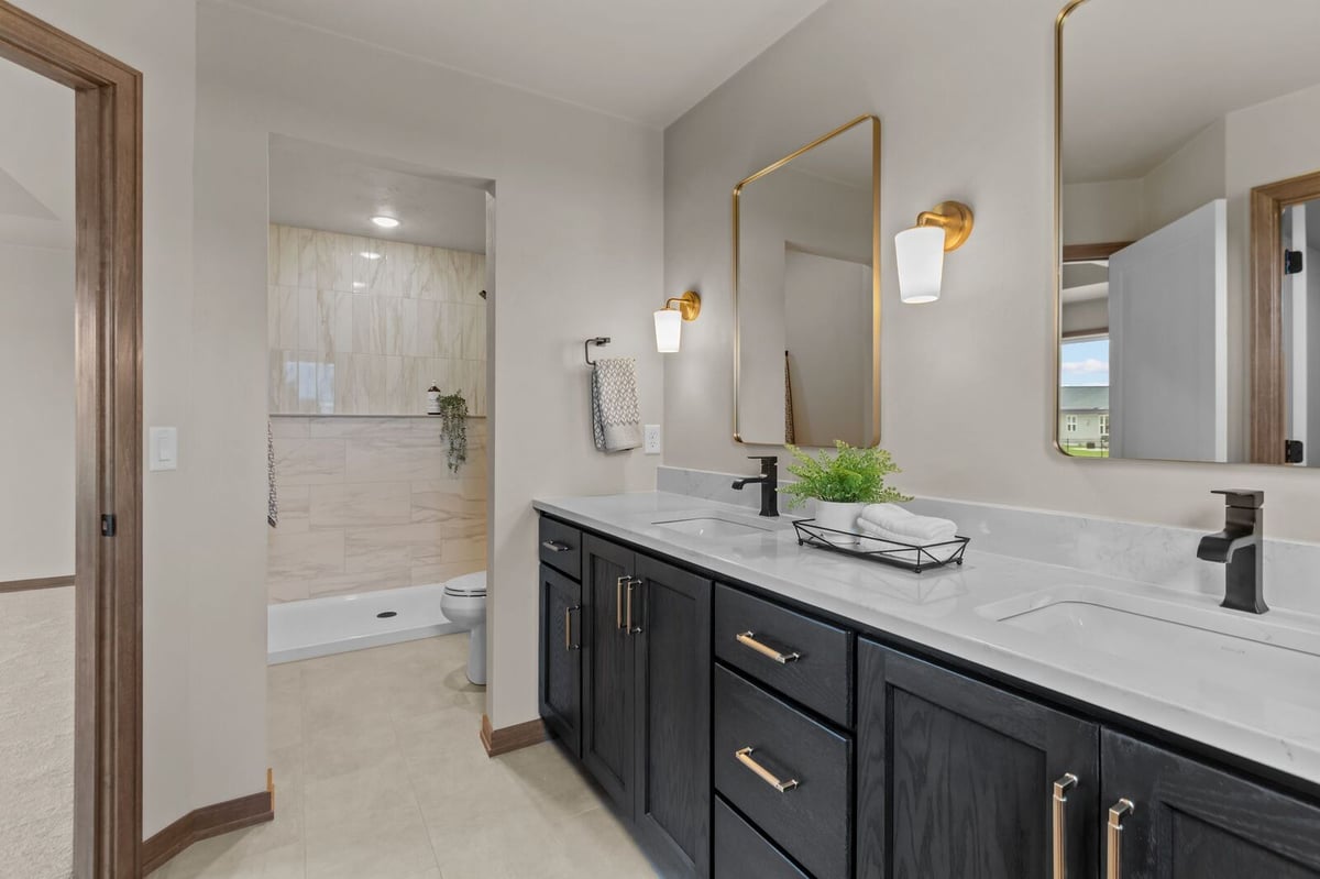 Modern Northern Wisconsin bathroom with dual sinks, gold fixtures, and tiled walk-in shower