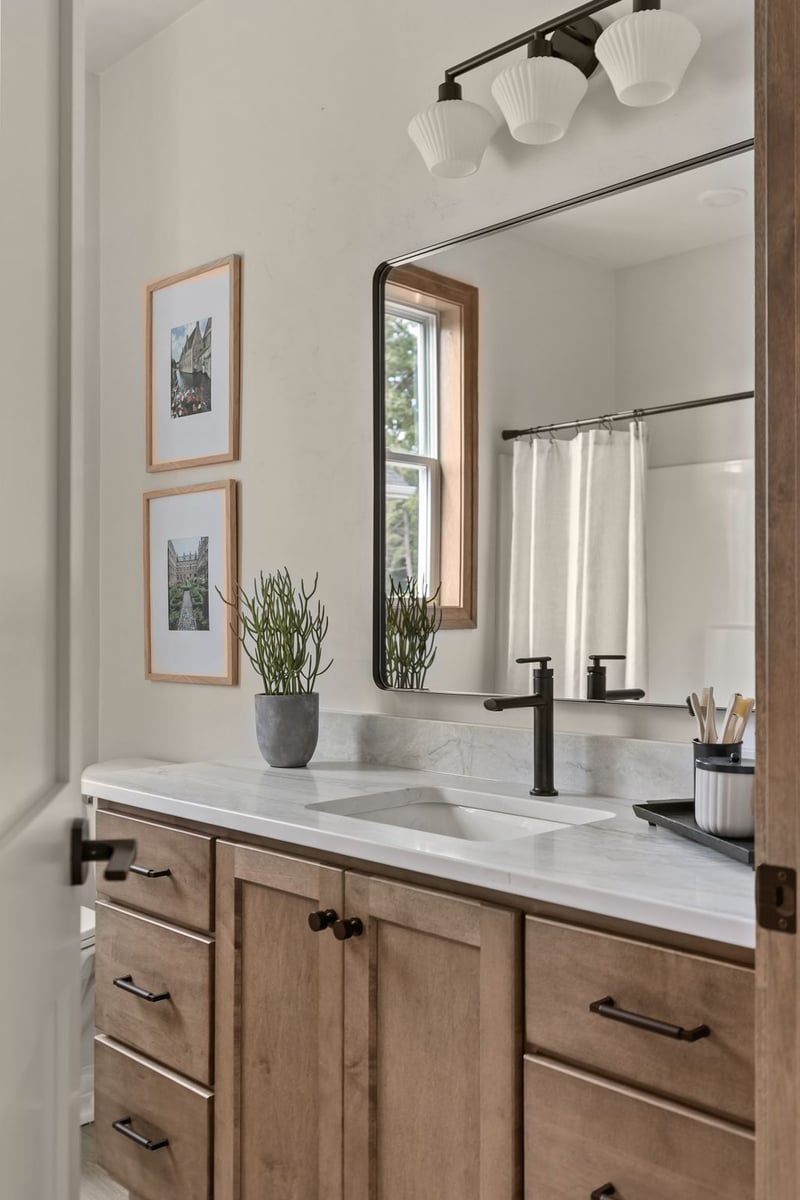 Bathroom vanity with wood cabinetry, black fixtures and large mirror in a Northeast Wisconsin home