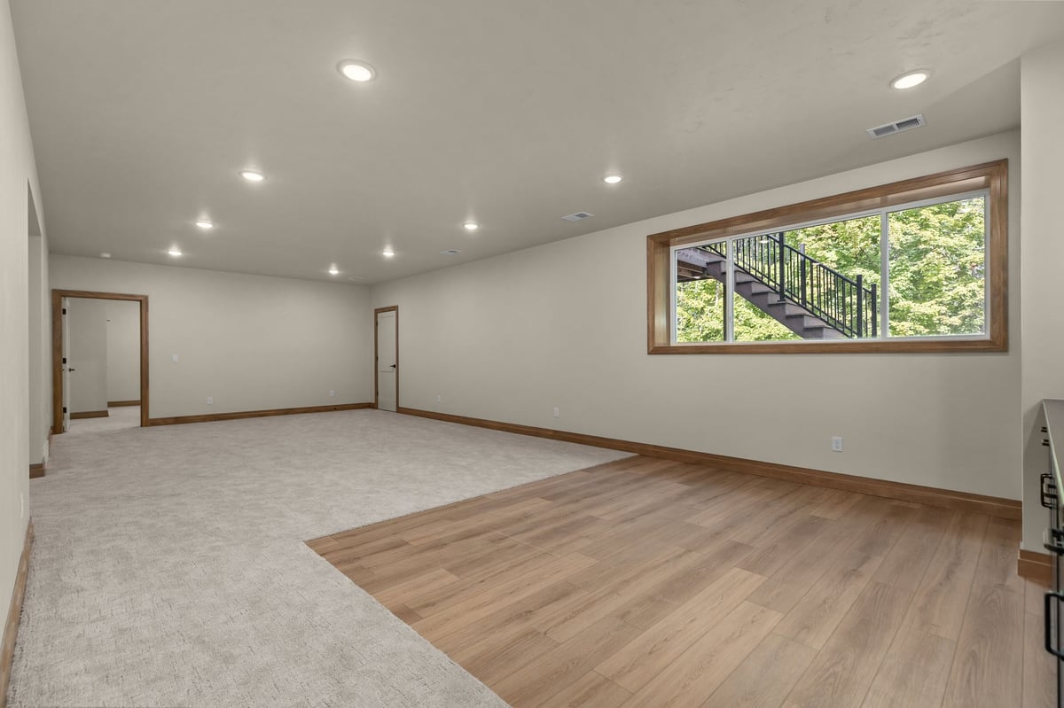 Finished lower-level recreation room with carpet, wood-look flooring and large window in a Northeast Wisconsin home