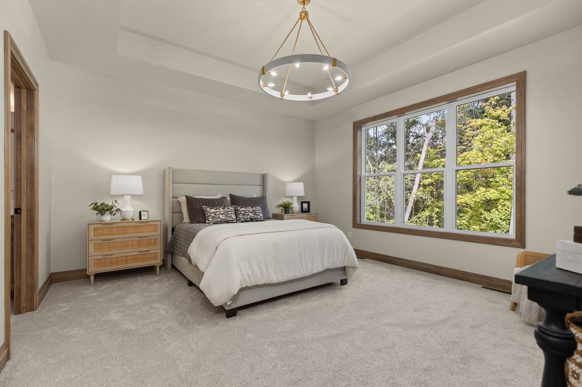 Northeast Wisconsin bedroom with large wooded-view windows, tray ceiling and modern chandelier