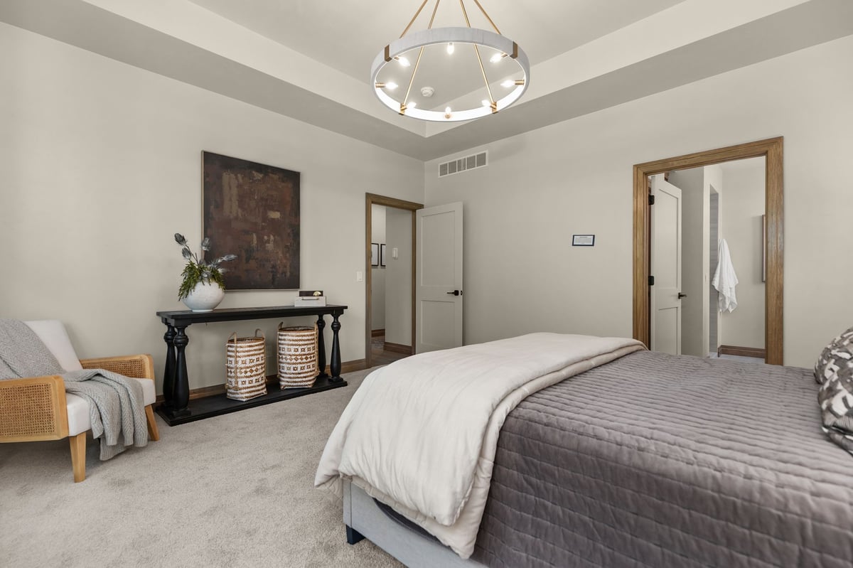 Primary bedroom with tray ceiling, modern chandelier and warm wood trim in a Northeast Wisconsin home