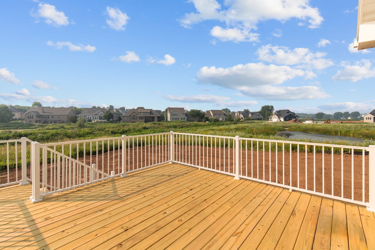 Appleton, WI backyard deck with wood flooring, white railing, and open views of nearby homes and green space under blue sky