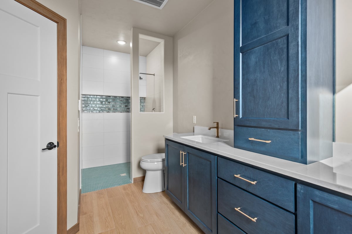Appleton, WI bathroom with blue vanity, white countertop, gold fixtures, and walk-in shower with blue accent tile