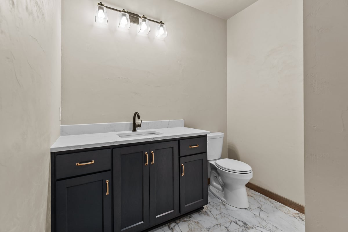 Appleton, WI bathroom with dark vanity, white countertop, gold hardware, modern lighting, and marble-look tile flooring