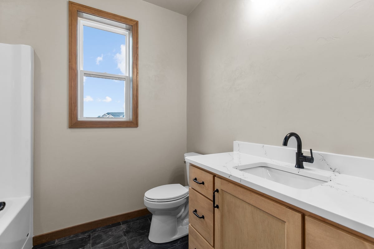 Appleton, WI bathroom with wood vanity, white countertop, black faucet, window for natural light, and dark tile flooring
