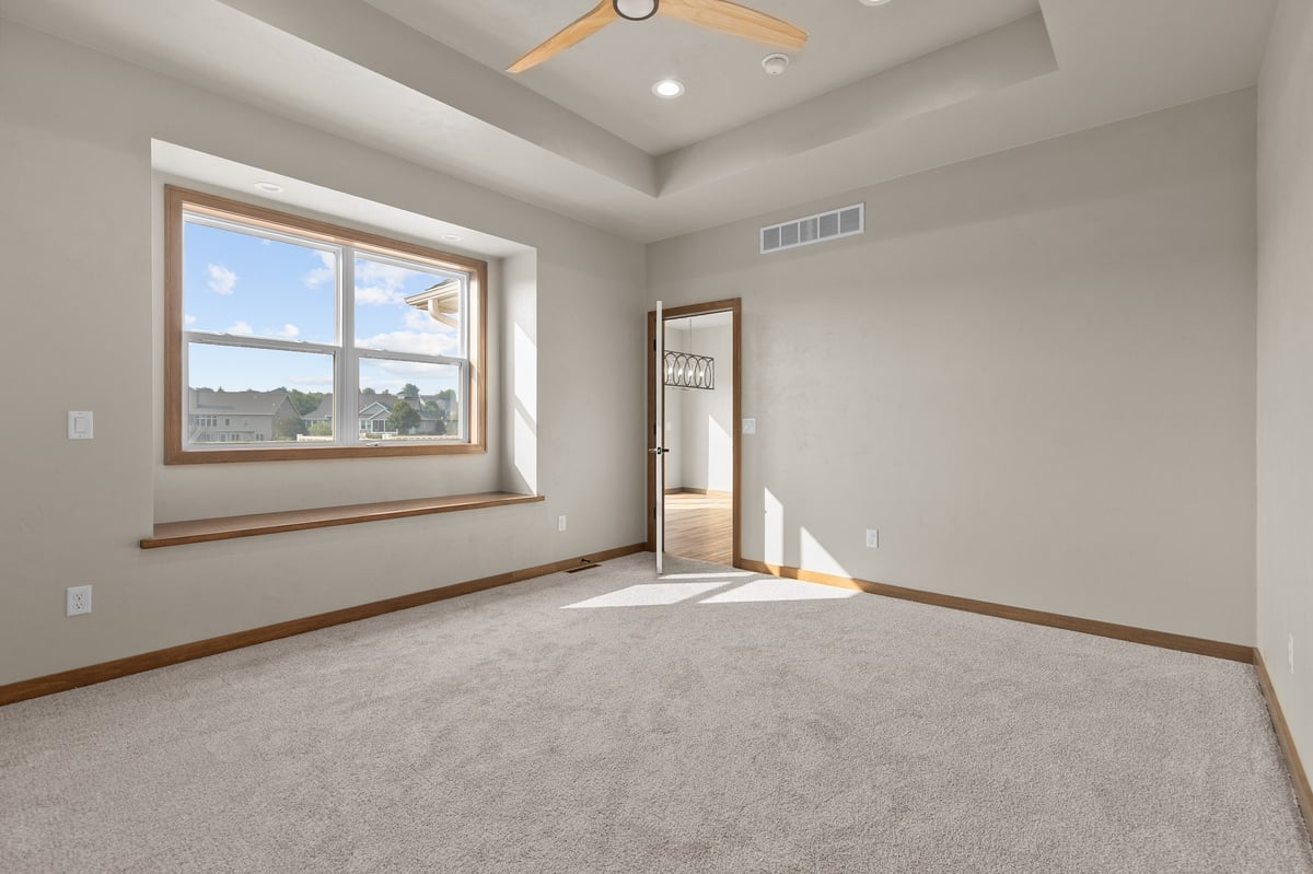 Appleton, WI bedroom with carpet, tray ceiling, ceiling fan, large window, and doorway to ensuite bathroom