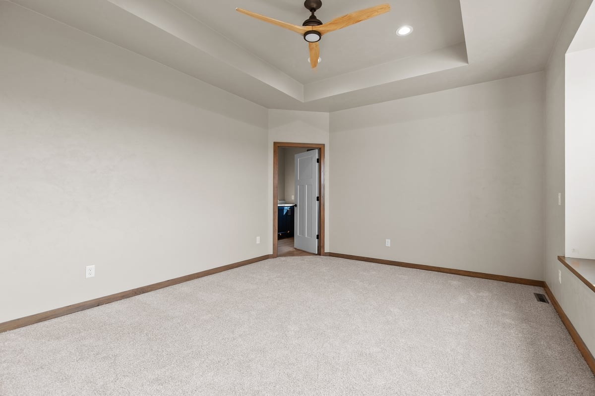 Appleton, WI bedroom with carpet, tray ceiling, ceiling fan, neutral walls, and doorway leading to an ensuite bathroom