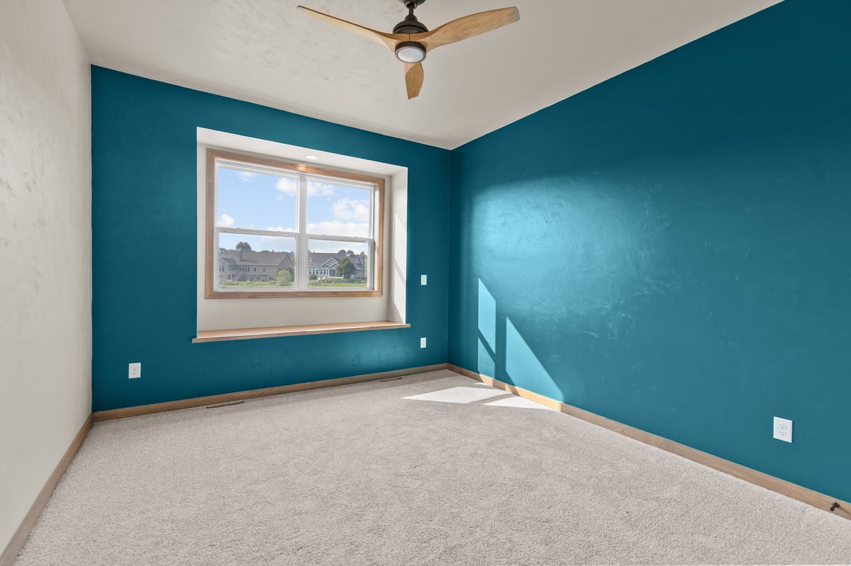 Appleton, WI bedroom with teal accent wall, carpet flooring, ceiling fan, and window providing natural light
