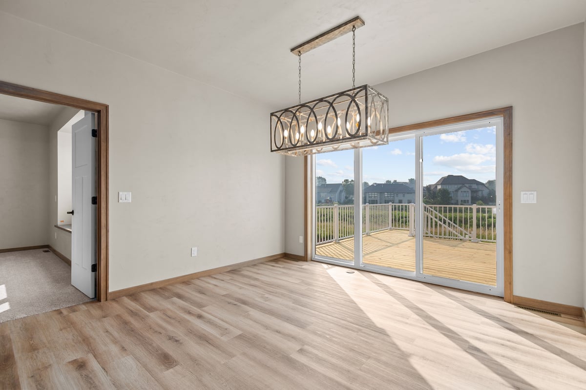 Appleton, WI dining room with modern chandelier, wood floors, and sliding glass doors leading to a deck with backyard views