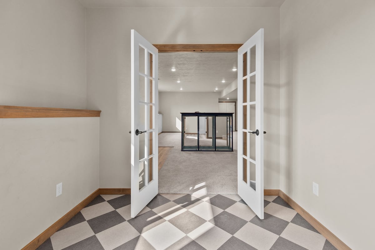 Appleton, WI entry with double French doors opening to a lower-level living space, featuring checkered tile flooring and natural wood trim
