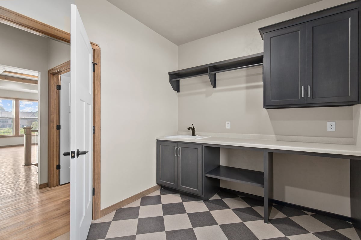 Appleton, WI laundry room with dark cabinets, utility sink, folding counter, open shelving, and checkered tile flooring