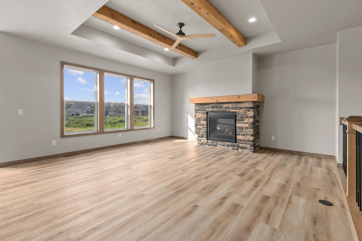 Appleton, WI living room with large windows, wood beam ceiling, ceiling fan, stone fireplace, and open layout with wood flooring