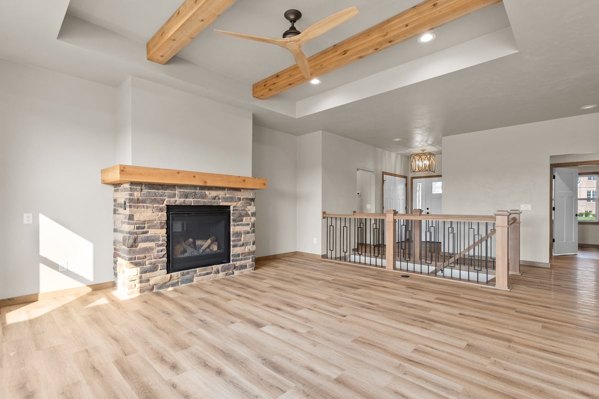 Appleton, WI living room with stone fireplace, wood beam ceiling, modern fan, and open railing overlooking lower level