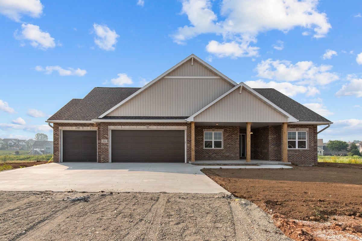 Appleton, WI new construction home exterior with brick facade, three-car garage, and freshly graded yard under blue sky