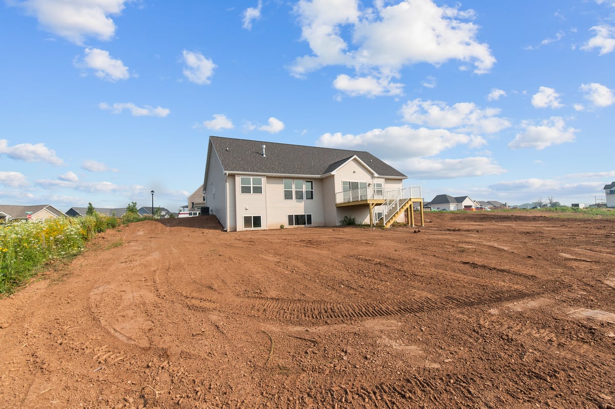 Appleton, WI rear view of home with large yard, elevated deck, and open landscape under a bright blue sky