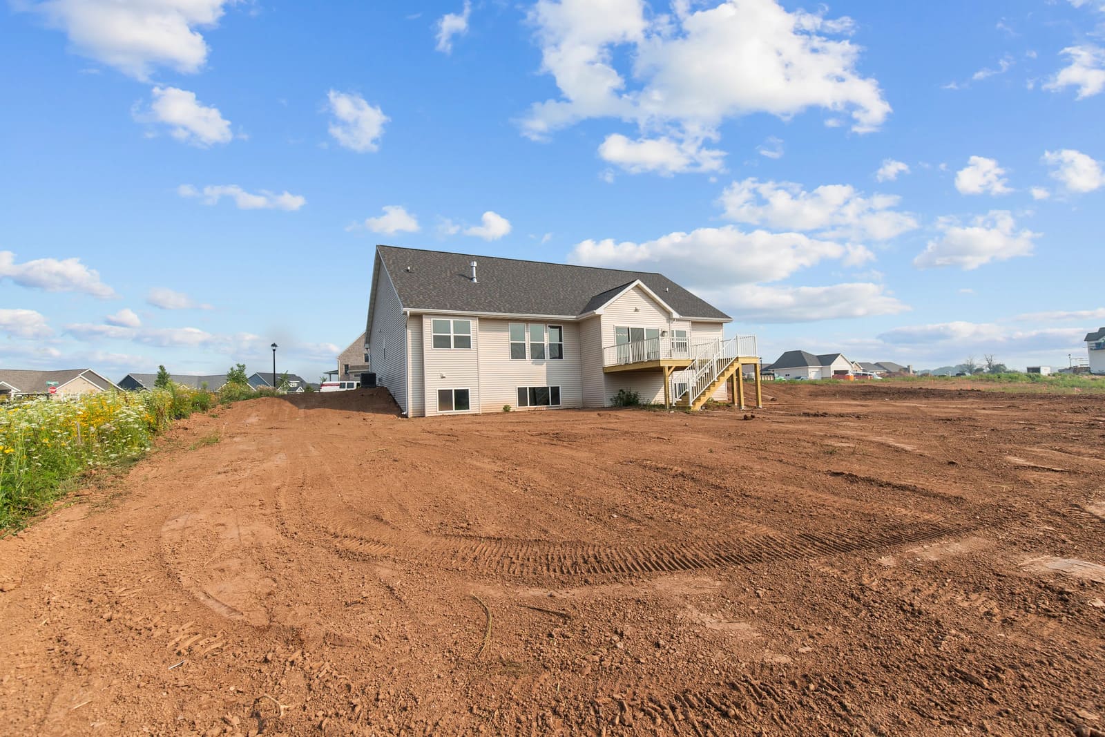 Appleton, WI rear view of home with large yard, elevated deck, and open landscape under a bright blue sky Appleton, WI rear view of home with large yard, elevated deck, and open landscape under a bright blue sky