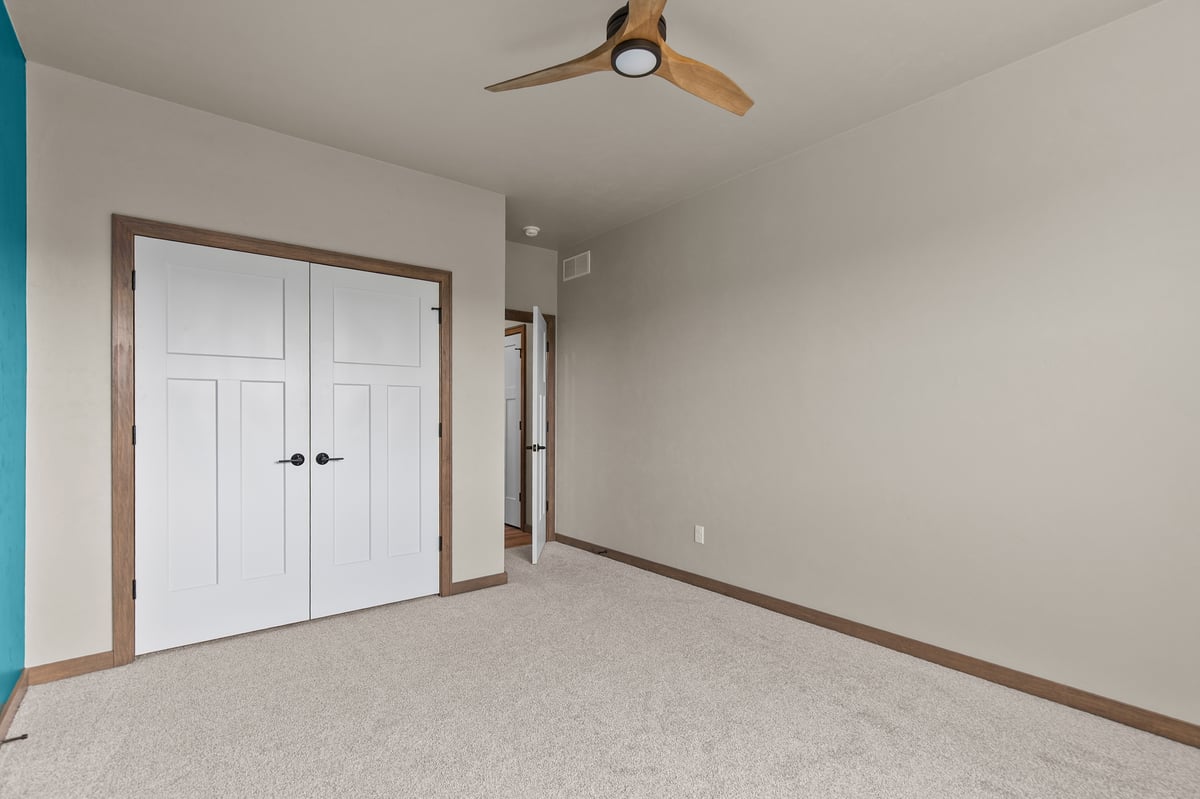 Bedroom in Appleton, WI with carpet, ceiling fan, double closet doors, and neutral walls with wood trim