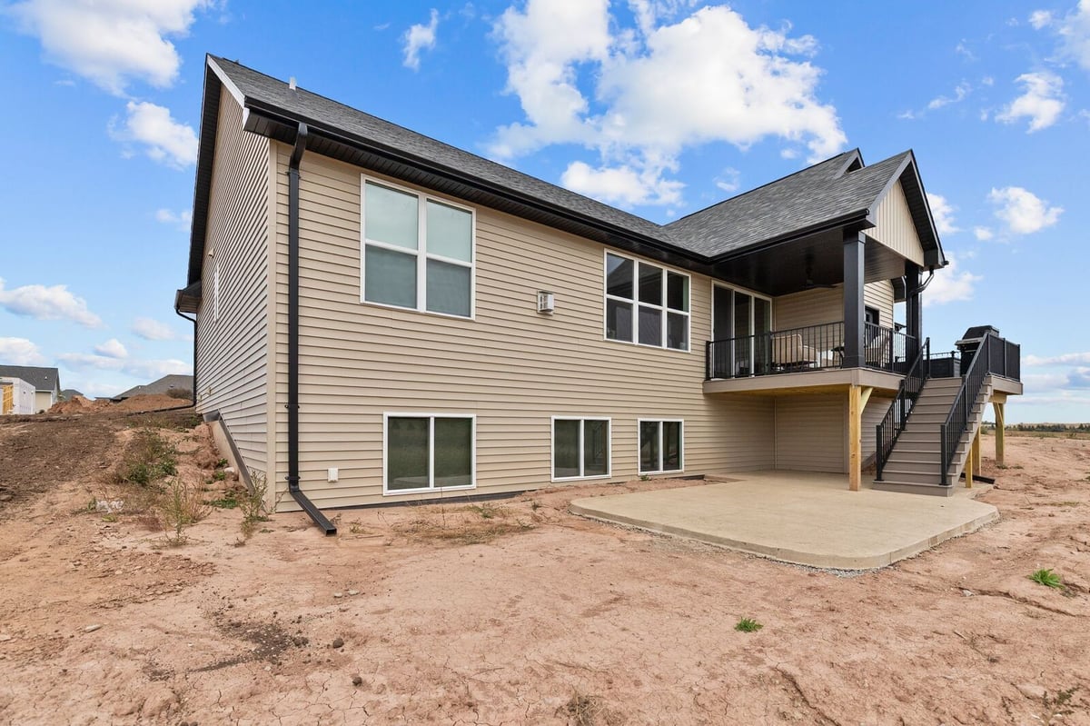 Appleton, WI backyard view of new beige house with raised deck, stairs, and concrete patio on unfinished dirt lot