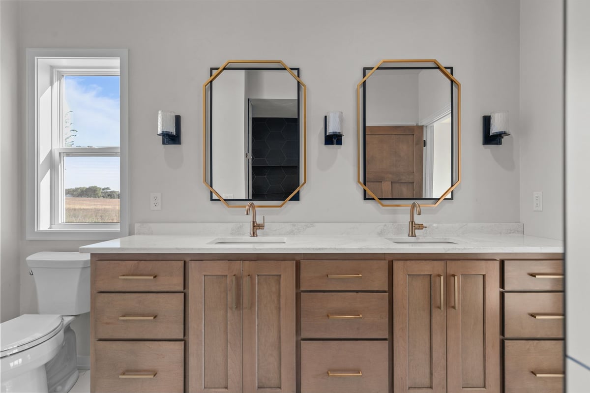 Appleton, WI bathroom with double vanity, wood cabinets, dual mirrors, gold fixtures, and natural light