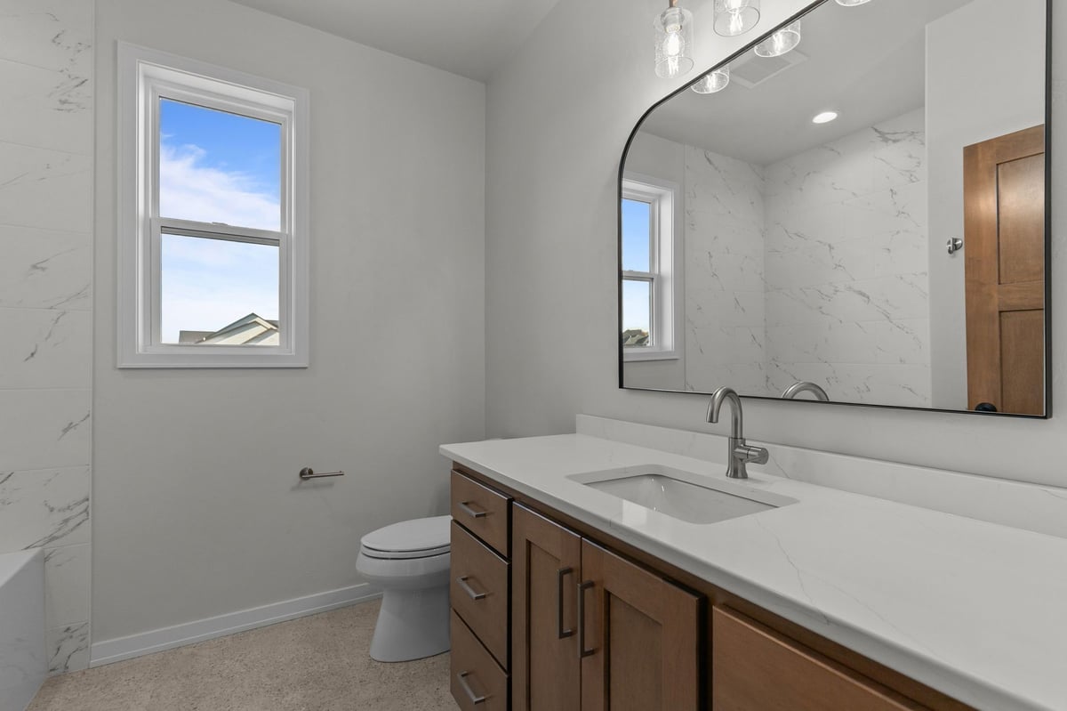Appleton, WI bathroom with single vanity, large mirror, marble-look shower walls, and window for natural light