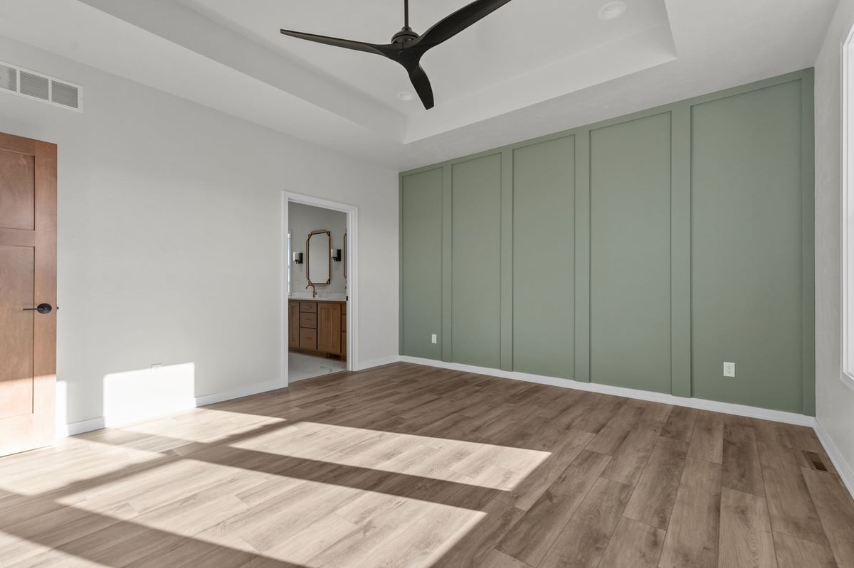 Appleton, WI bedroom with green accent wall, wood flooring, ceiling fan, and doorway to bathroom