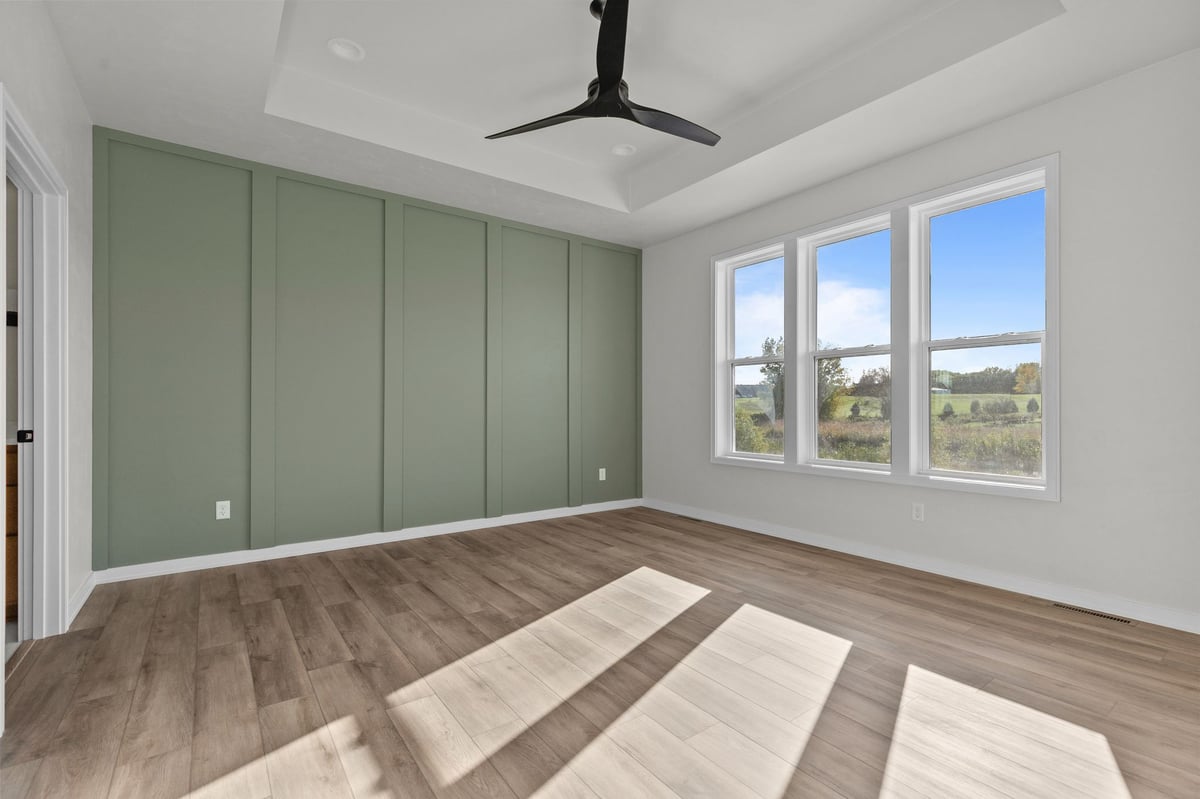 Appleton, WI bright bedroom with green accent wall, large windows, ceiling fan, and wood flooring