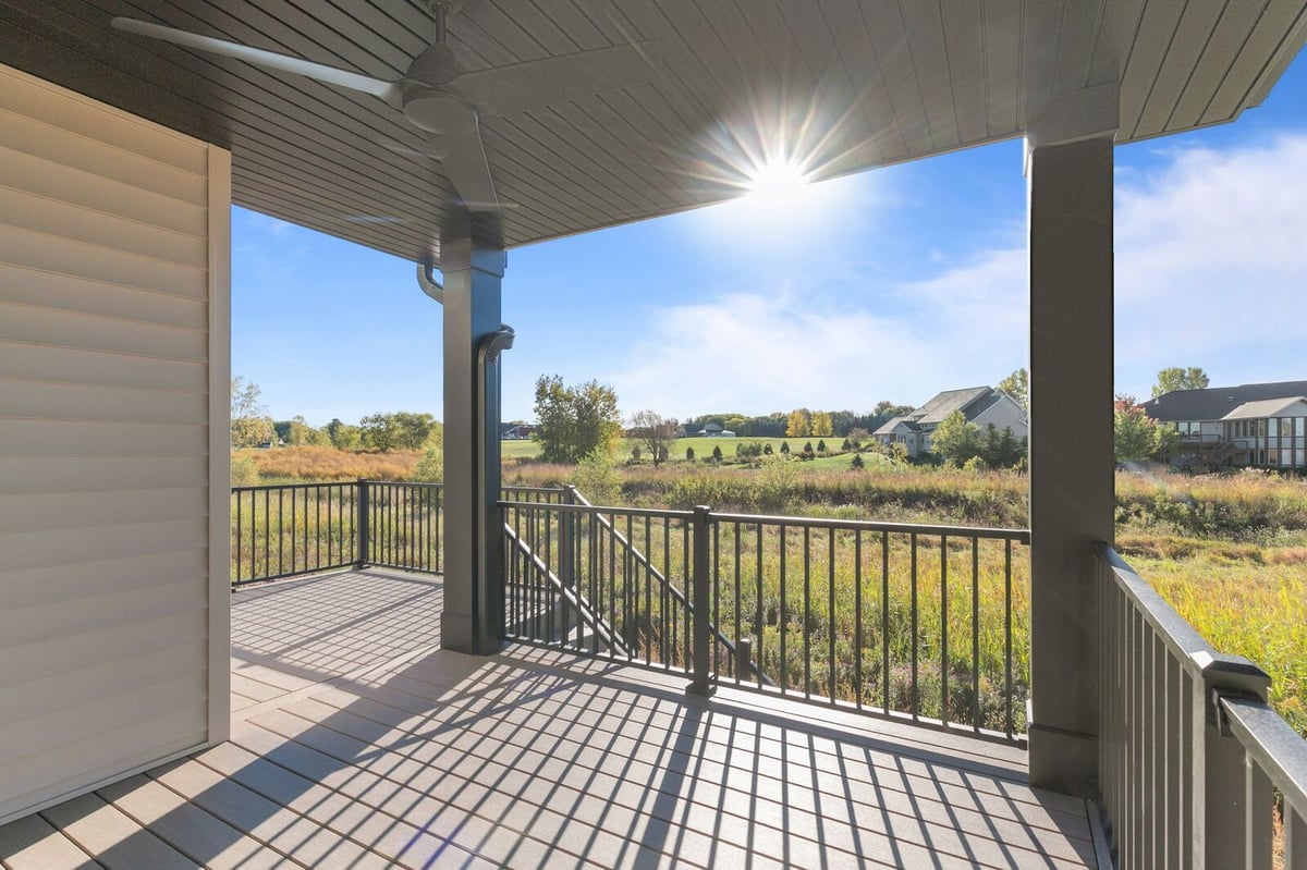 Appleton, WI covered deck with railing and ceiling fan overlooking open grassy field and neighboring homes in bright sunlight