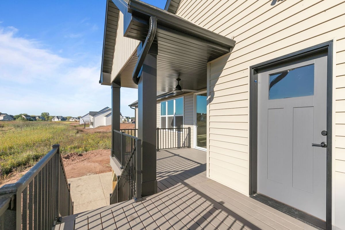 Appleton, WI covered deck with railing, ceiling fan, and backyard views of open field and neighboring homes