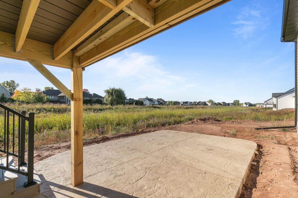 Appleton, WI covered patio beneath deck with wood posts and concrete slab facing open field and neighboring houses