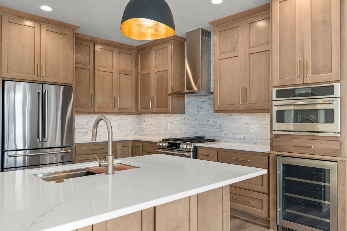 Appleton, WI kitchen detail showing large island, wood cabinetry, stainless fridge, range, and built-in oven with warm pendant light