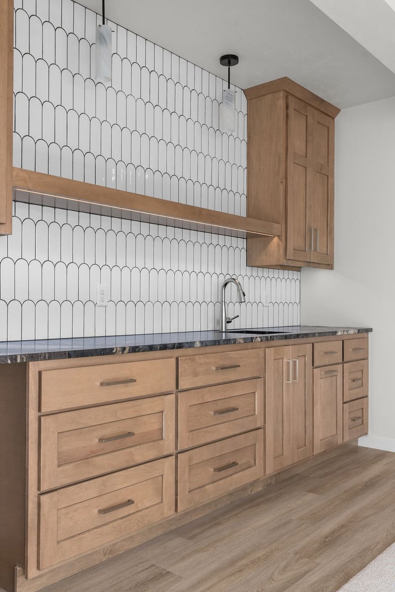 Appleton, WI kitchenette with wood cabinets, dark countertop, white scalloped tile backsplash, and pendant lighting