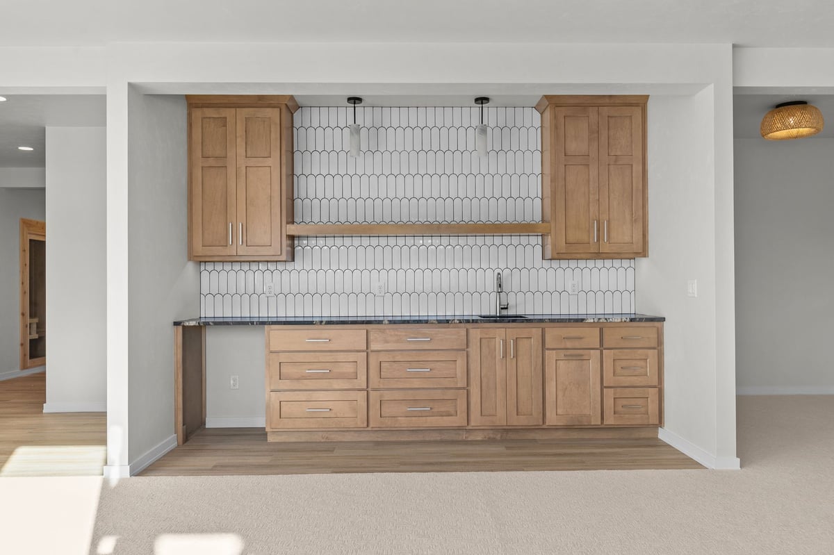 Appleton, WI lower-level wet bar with wood cabinets, tile backsplash, open shelving, and countertop sink in finished basement