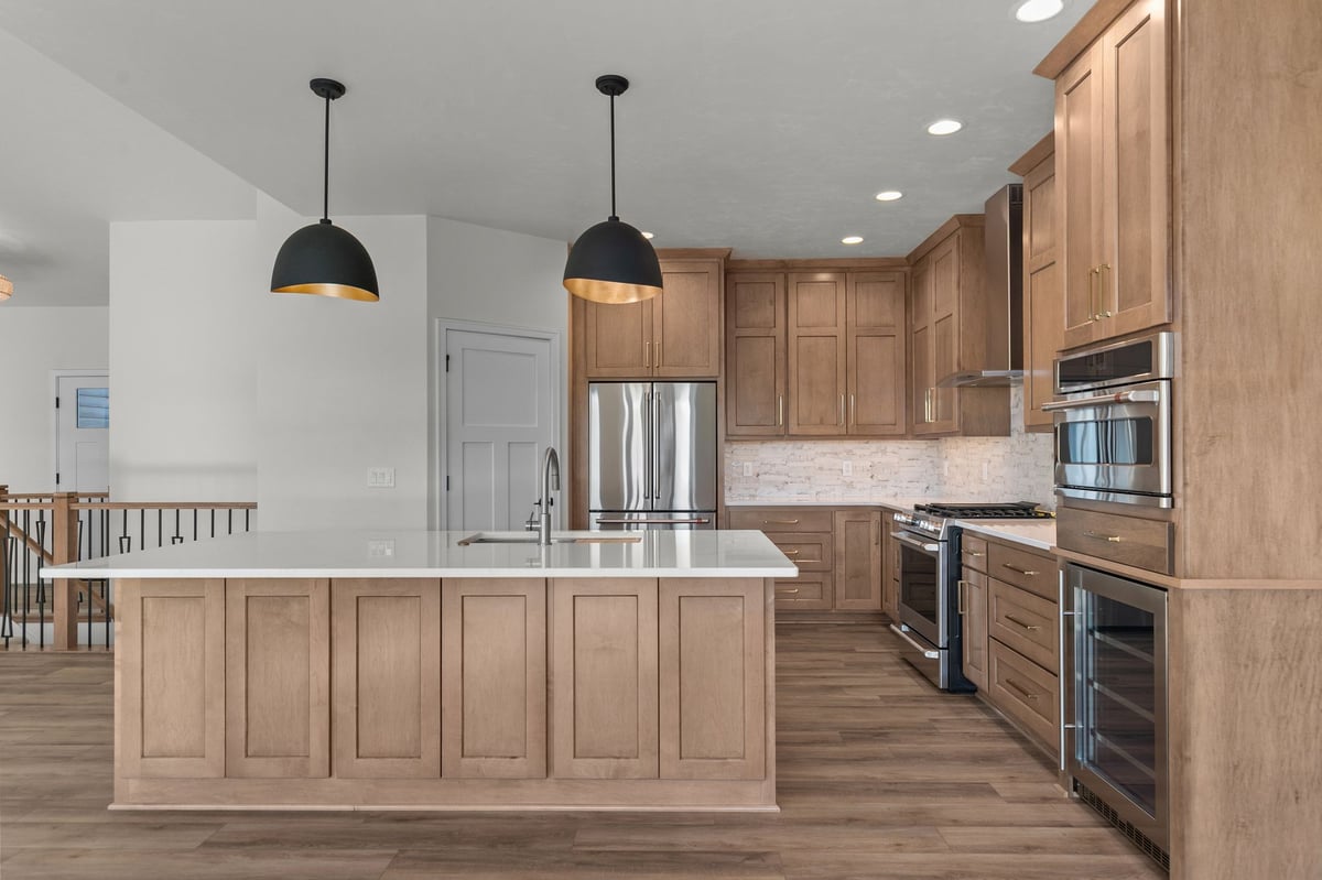 Appleton, WI modern kitchen with large island, wood cabinetry, white countertops, stainless appliances, and black pendant lighting