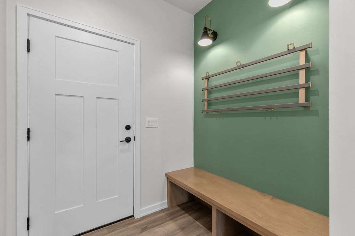Appleton, WI mudroom with green accent wall, wood bench, coat rack, and white door entry