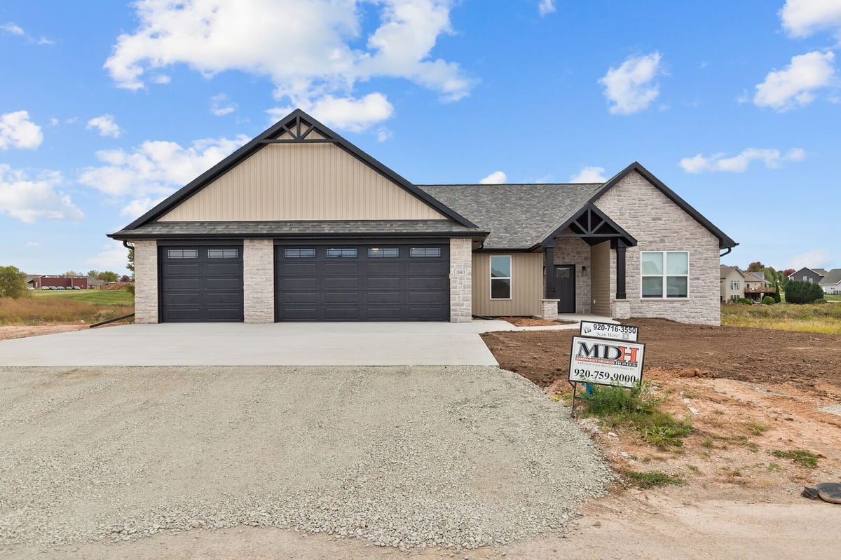 Appleton, WI new construction home exterior with three-car garage, stone accents, and unfinished yard and driveway