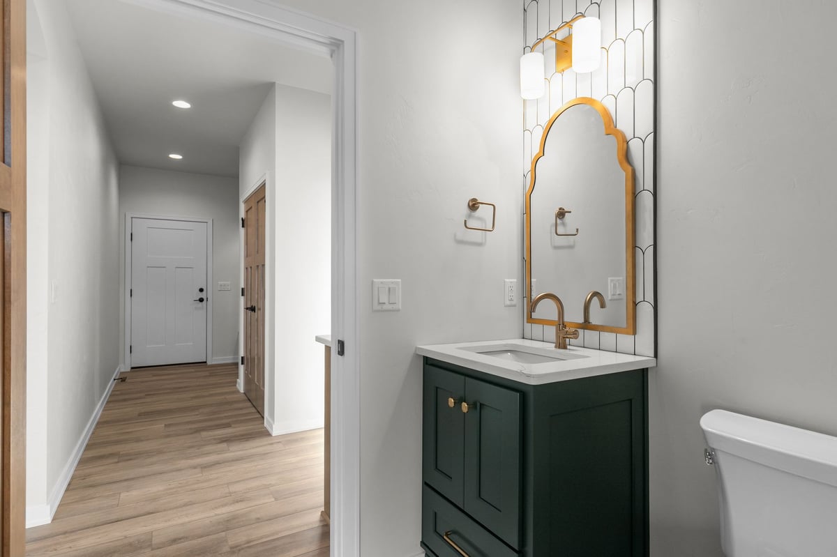 Appleton, WI powder room with green vanity, gold mirror, modern lighting, and adjacent hallway with wood flooring