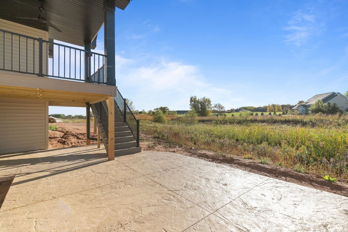 Appleton, WI rear exterior showing elevated deck, stairs, and large concrete patio beside open grassy landscape