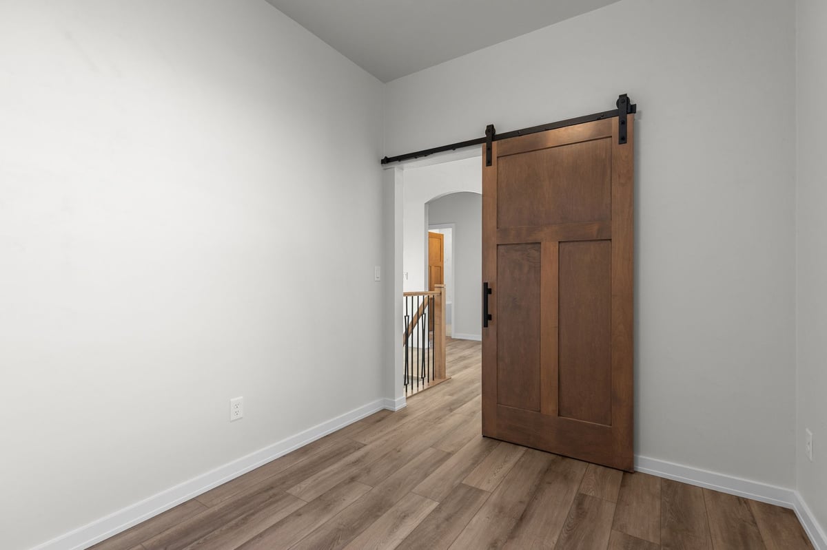 Appleton, WI room with sliding barn door, wood flooring, and open view to hallway and railing