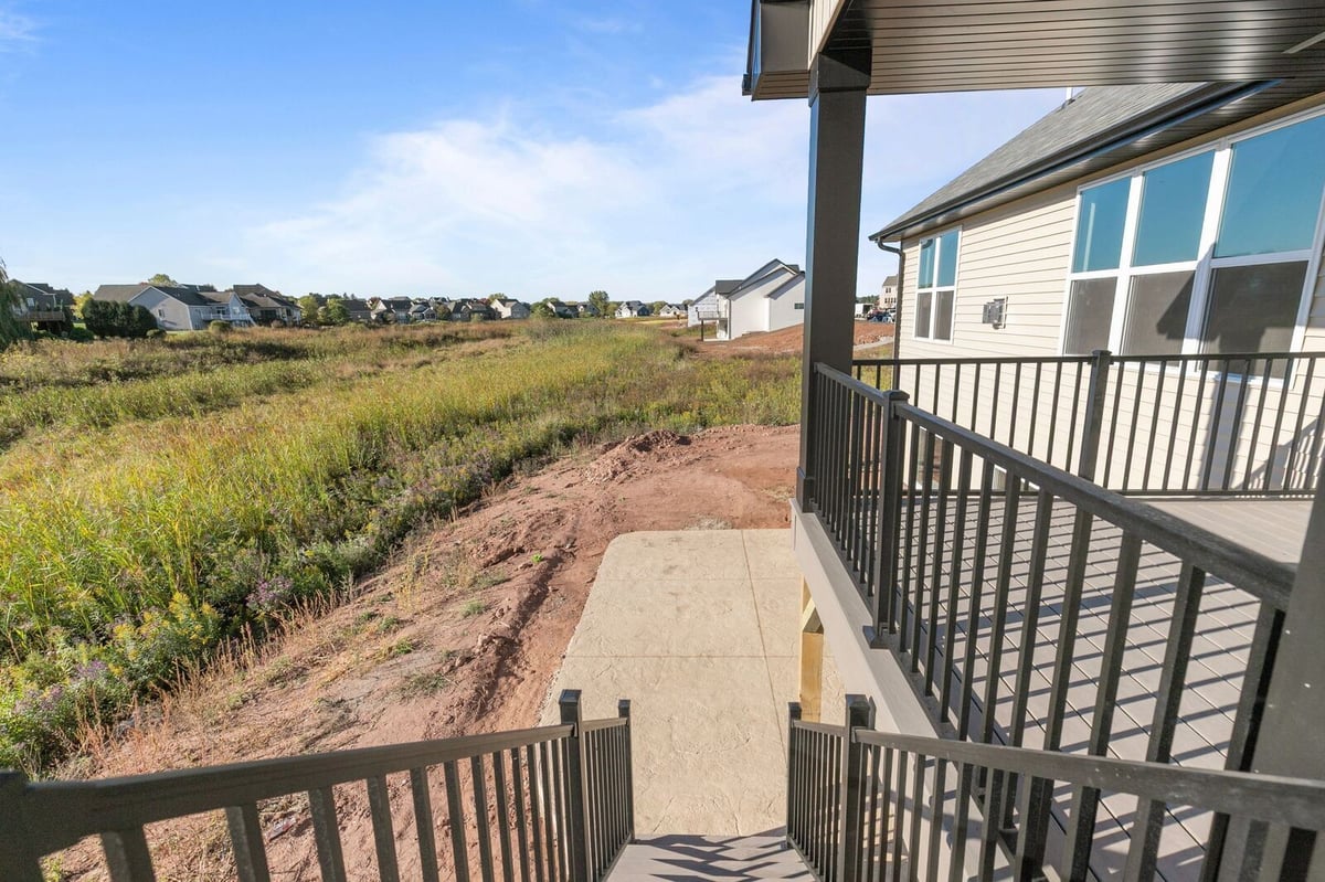 Appleton, WI view from deck stairs overlooking backyard, concrete patio, and open grassy field with nearby homes