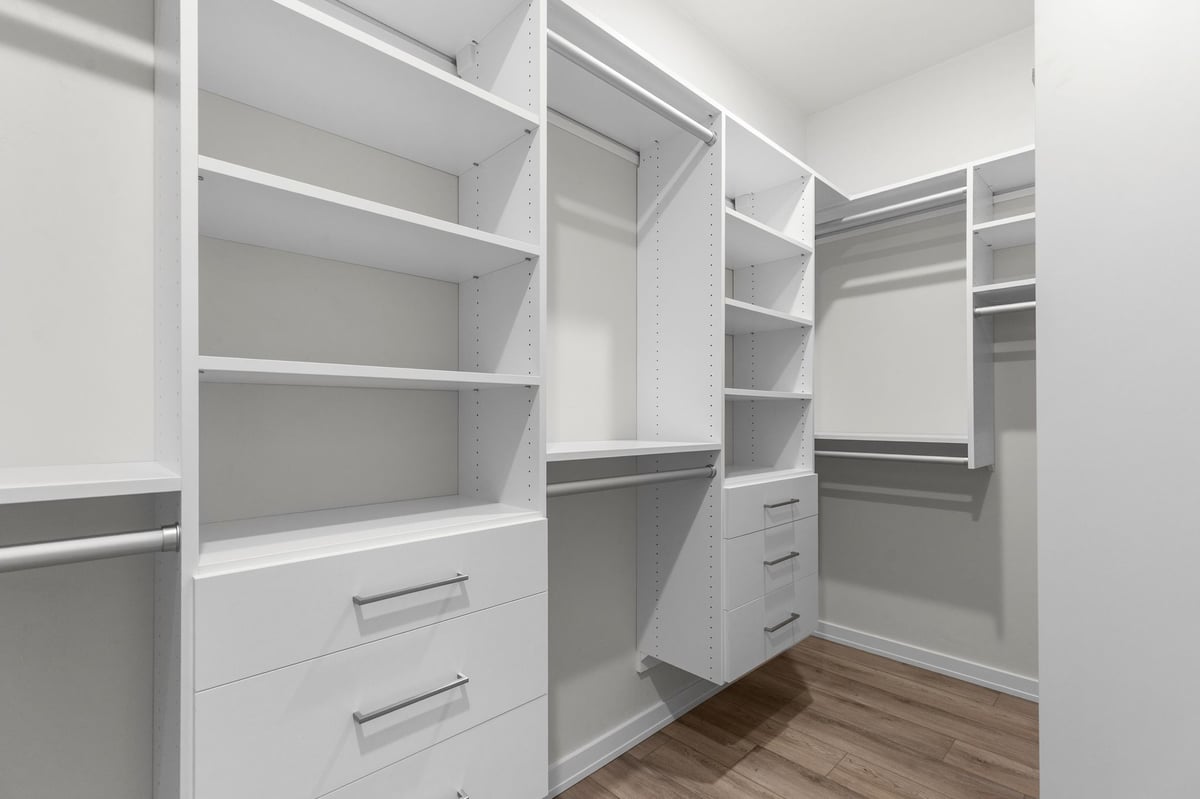 Appleton, WI walk-in closet with white built-in shelving, drawers, and hanging rods on wood flooring