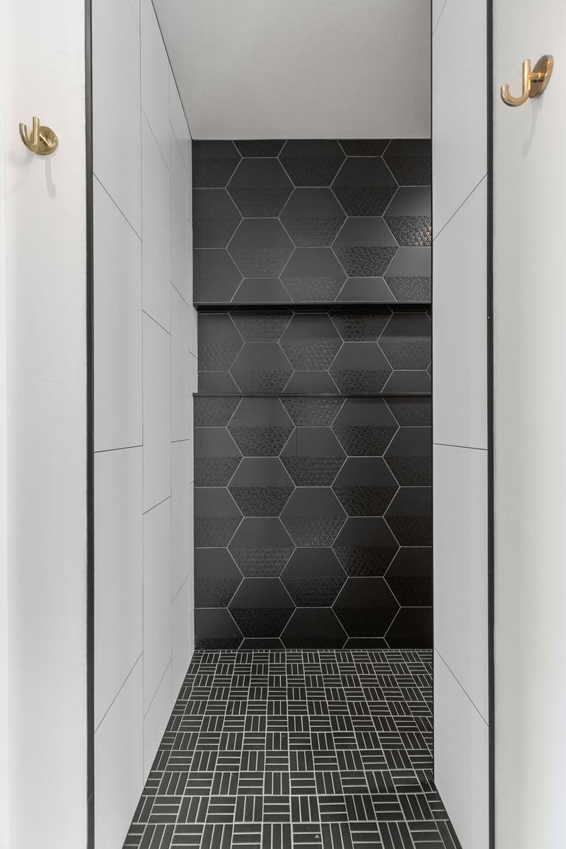 Appleton, WI walk-in shower with black hex tile accent wall, white tile sides, and patterned tile floor