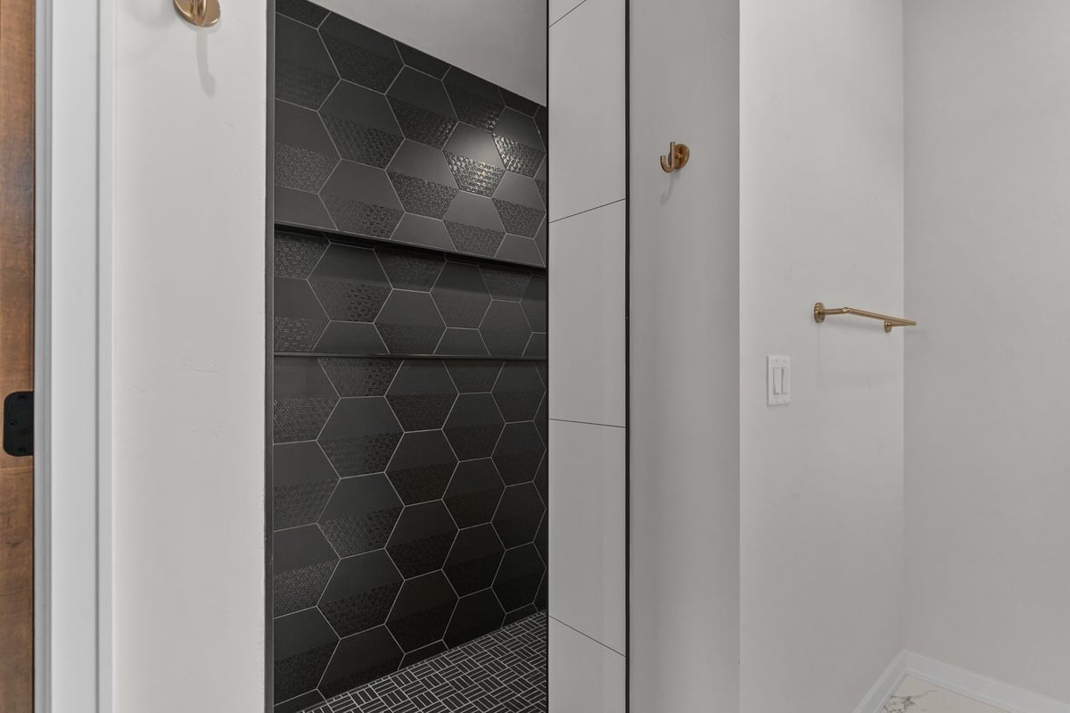 Appleton, WI walk-in shower with black hex tile, built-in shelves, and modern gold fixtures
