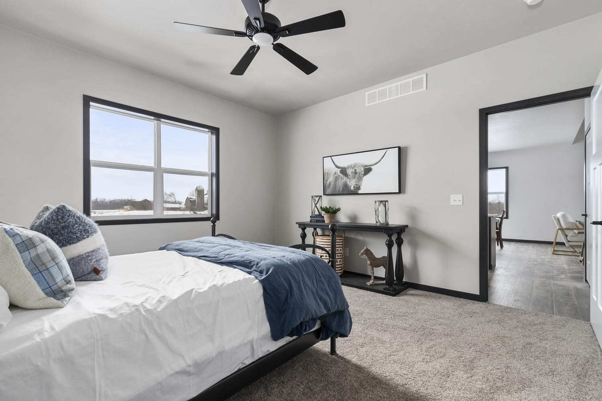 Cozy bedroom with a black ceiling fan, blue bedding, and farm views in the Fox Cities