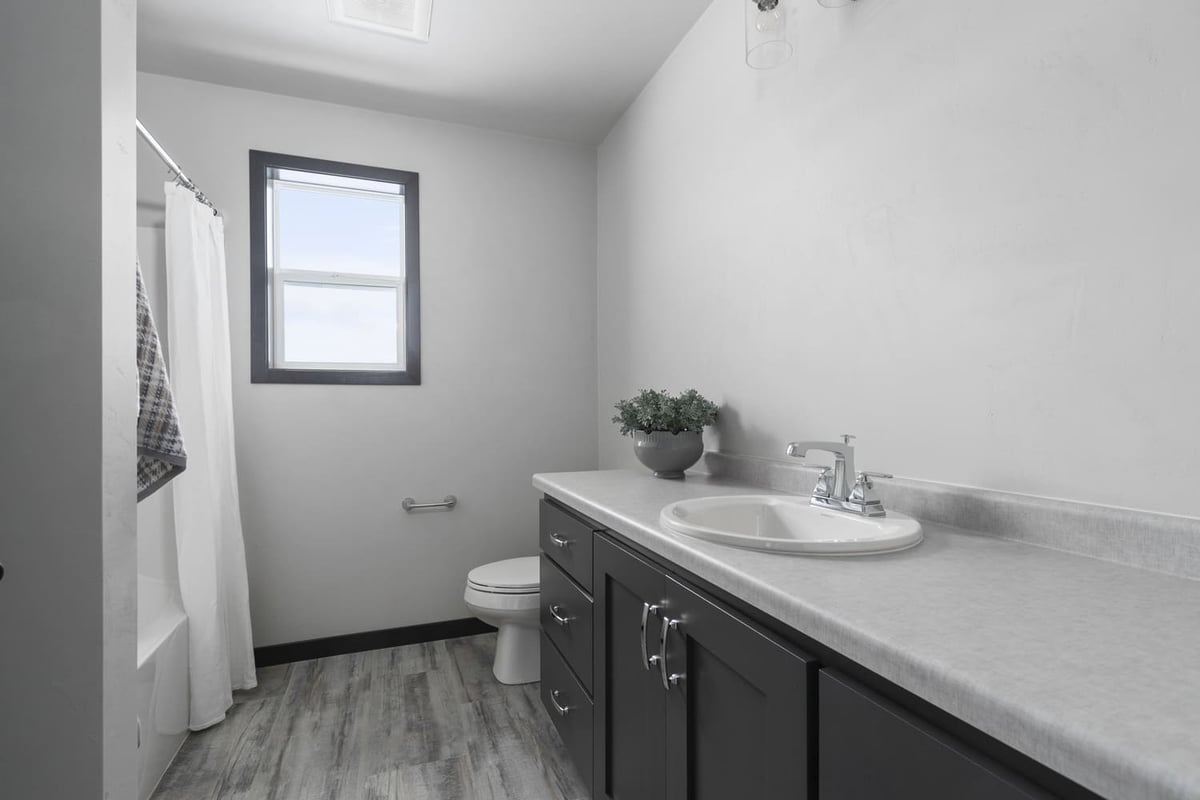 Full bathroom with dark vanity, tub shower, window, and vinyl flooring in a Fox Cities home