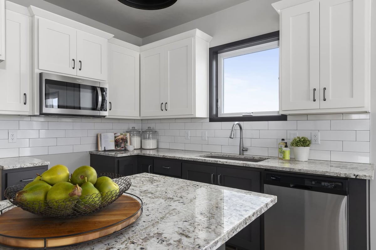 Modern kitchen with white cabinets, black lowers, granite island, and stainless appliances in a Fox Cities home