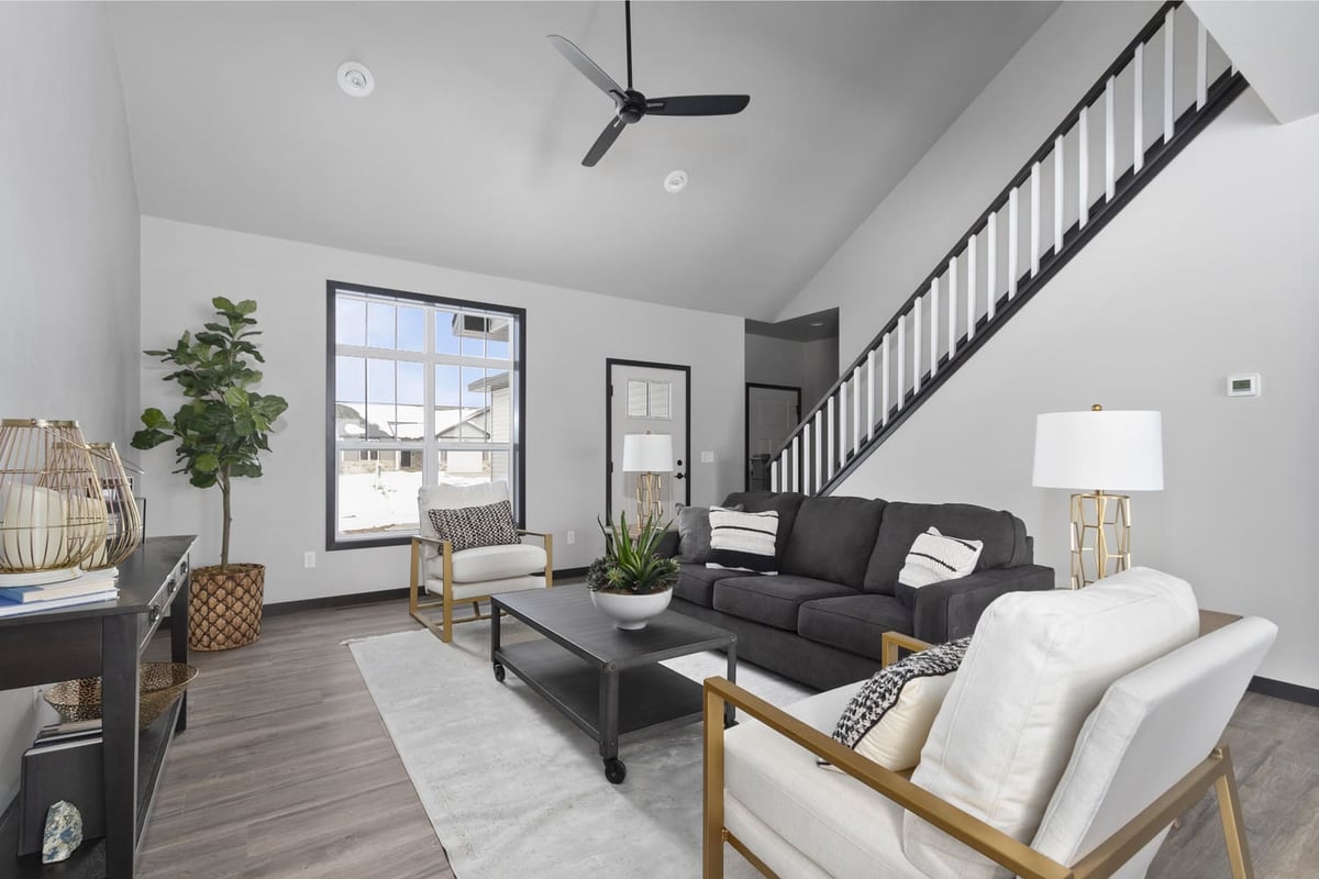 Modern living room in the Fox Cities with a vaulted ceiling, dark-railed staircase, and stylish white armchairs