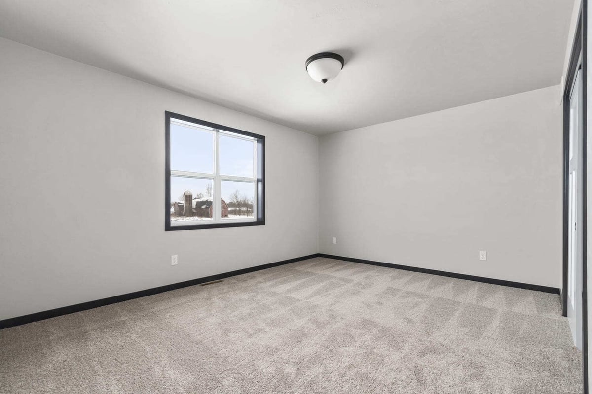 Spacious empty bedroom with neutral carpet and a window overlooking the Fox Cities landscape