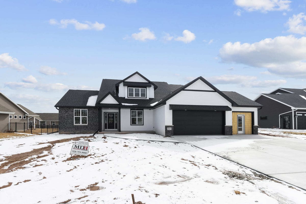 Front view of two-story home with black garage doors and stone accents, surrounded by snow in the Fox Cities