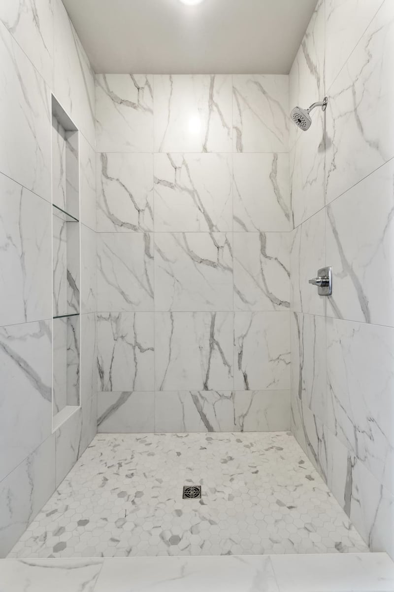 Shower with marble-style tile walls and hex tile floor in a Fox Cities home